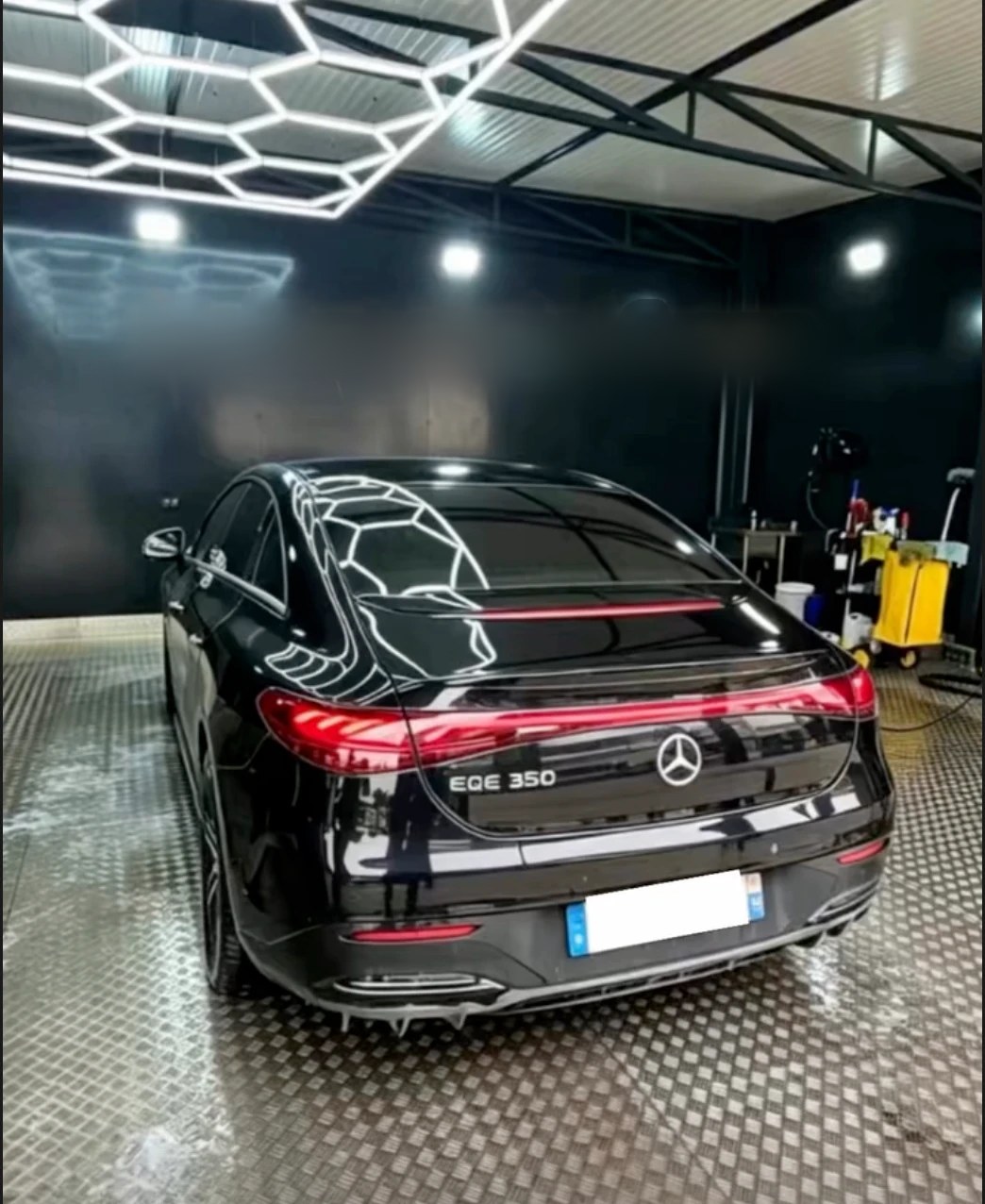 Berline noire dans le studio de lavage, sous le plafond de néons hexagonaux