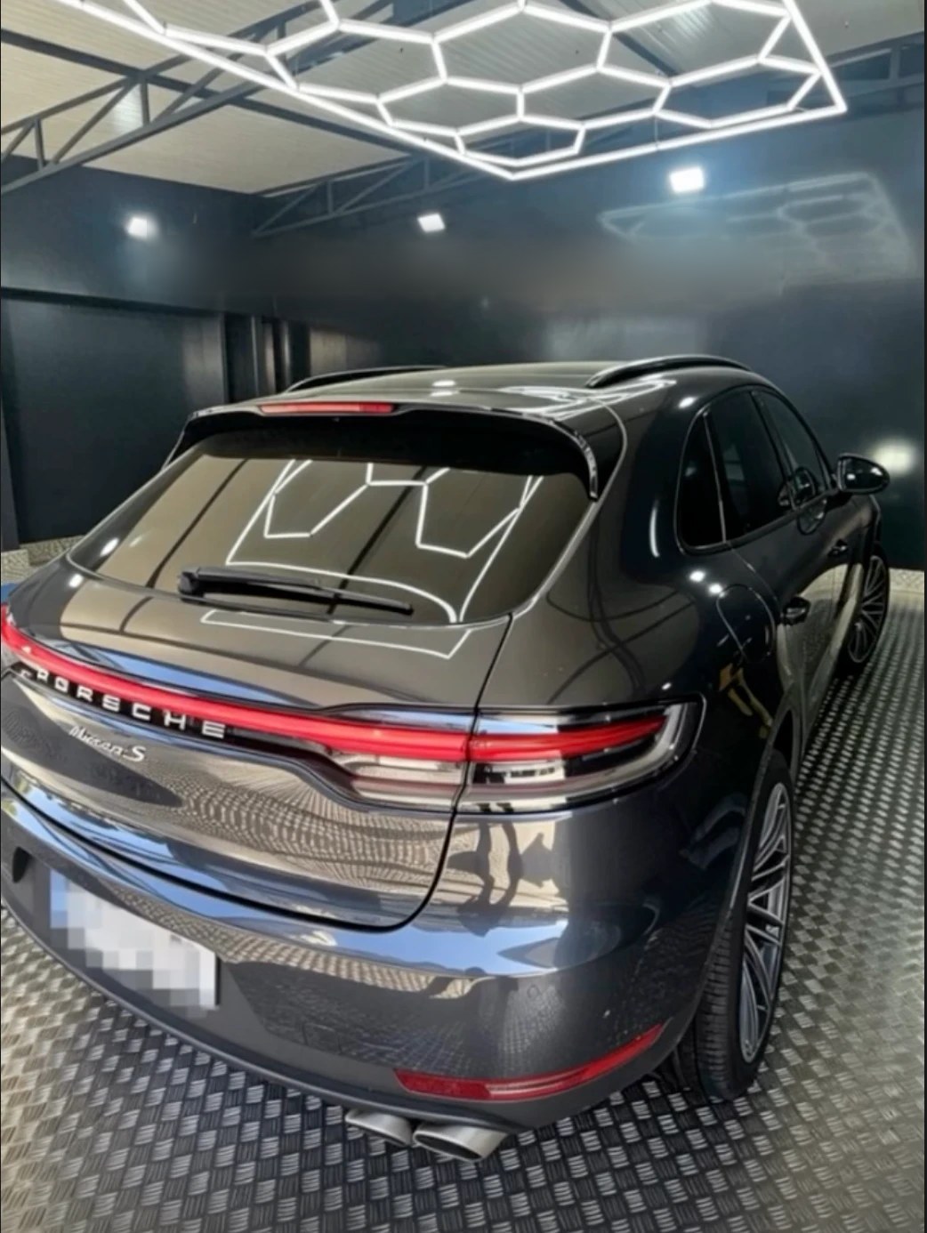 SUV gris anthracite après lavage, les néons du studio se reflètent sur la lunette arrière